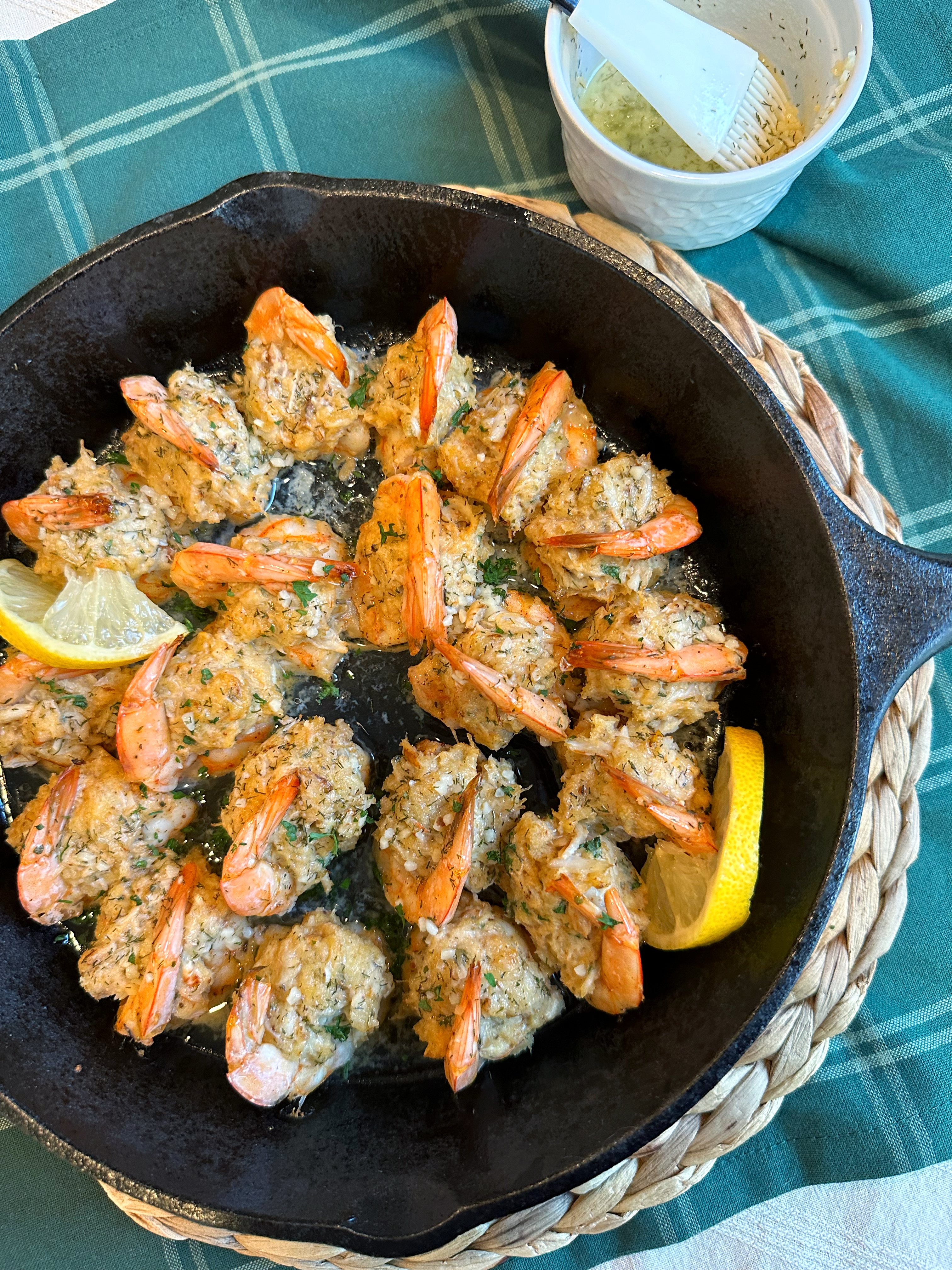 A cast-iron skillet filled with Crab Stuffed Shrimp, lemon slices, and fresh parsley and melted butter on the side.