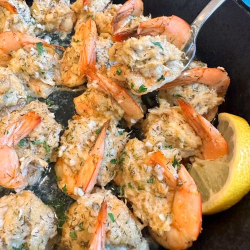 A cast-iron skillet filled with Crab Stuffed Shrimp, lemon slices, and fresh parsley.