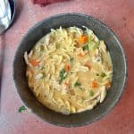 A bowl of creamy chicken noodle soup with egg noodles, carrots, creamy broth, and fresh parsley.