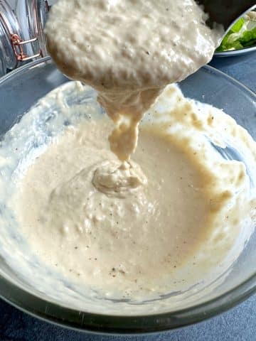 A spoon pouring homemade caesar dressing back into its bowl.