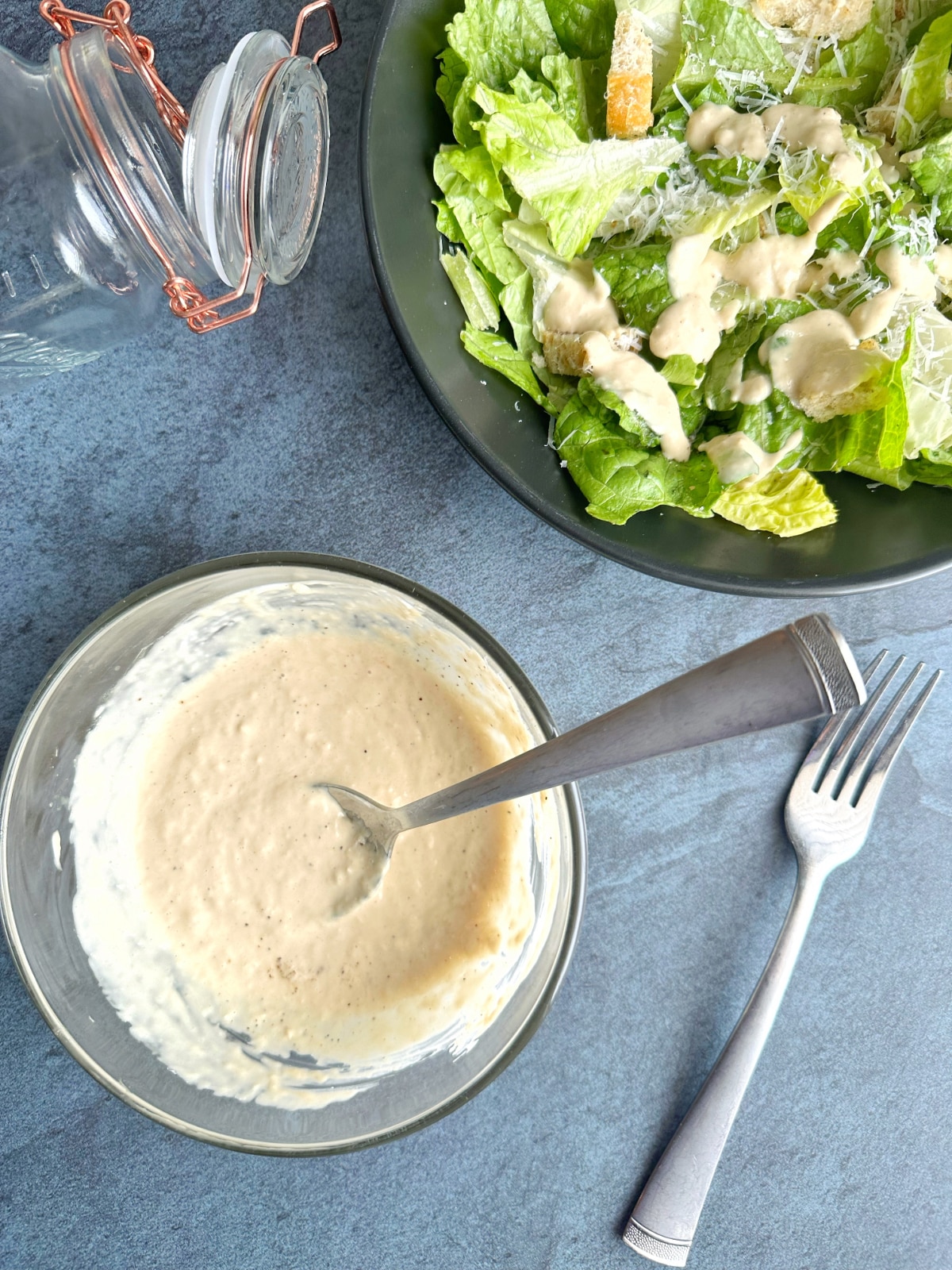 Homemade Caesar Dressing with a dressed Caesar salad and an empty mason jar on the side.