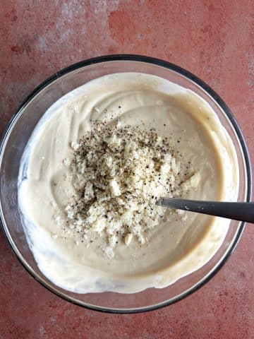 A glass bowl of homemade caesar salad dressing with extra cheese and black pepper on top.