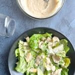 Homemade Caesar Dressing with a dressed Caesar salad and an empty mason jar on the side.