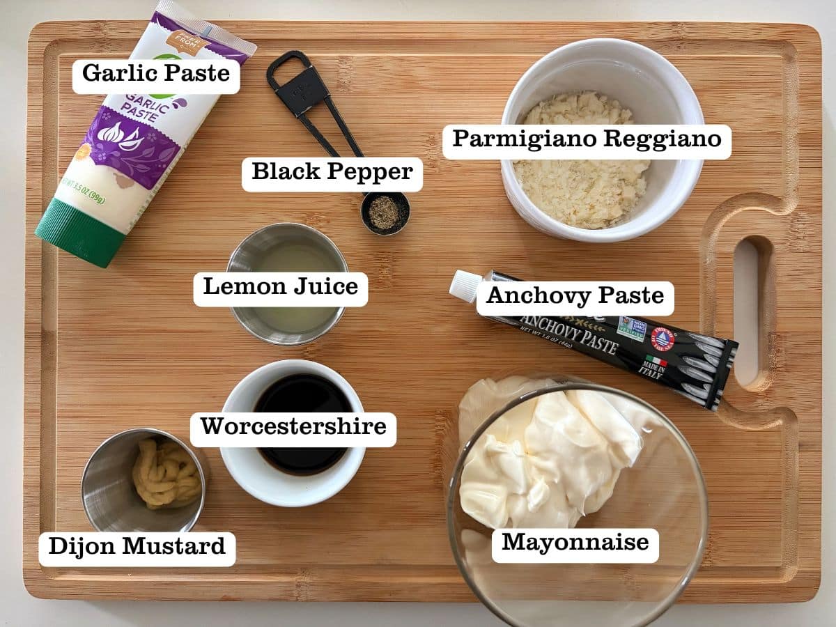 A wooden board with containers of ingredients for homemade caesar dressing with no eggs.