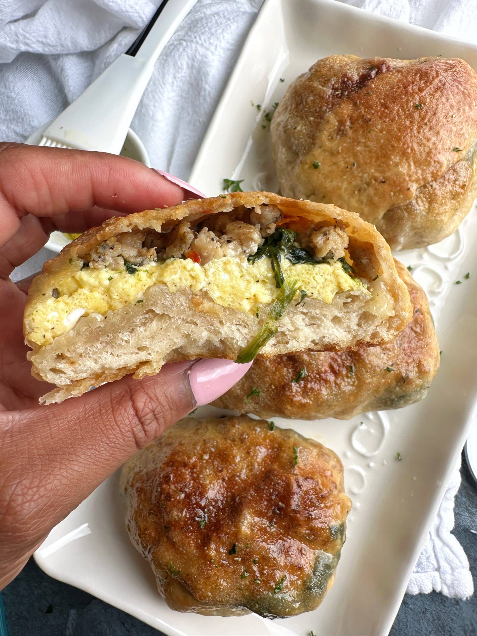 A hand holding a Sausage, Egg, Spinach, and Cheese Breakfast Pizza Pocket that's cut in half.