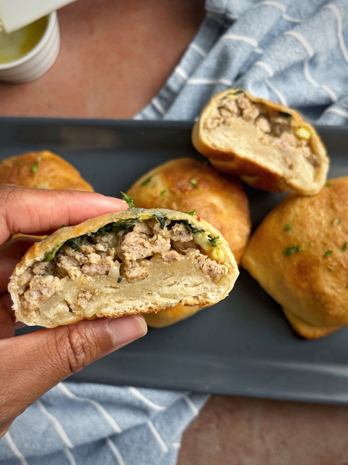 A hand holding up half of a breakfast pizza pocket with the remaining pastries in the background.