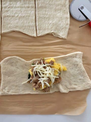 A rectangle of pizza dough with scrambled eggs, sausage, and cheese in the middle.