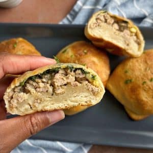 A hand holding a breakfast pizza pocket over a plate of more of them.