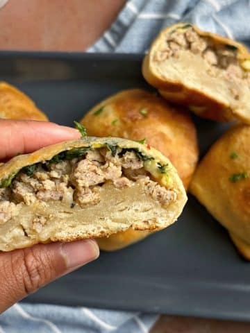 A hand holding a breakfast pizza pocket over a plate of more of them.
