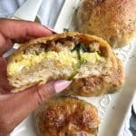 A hand holding a Sausage, Egg, Spinach, and Cheese Breakfast Pizza Pocket that's cut in half.