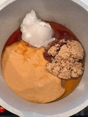 A saucepan filled with melted peanut butter, brown sugar, coconut oil, and syrup.