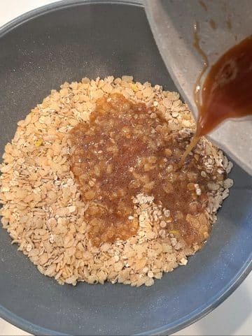 A pot of brown sugar syrup being poured onto a bowl of oats and puffed rice cereal.