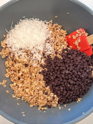 A mixing bowl filled with moist oats, mini chocolate chips, and shredded coconut.