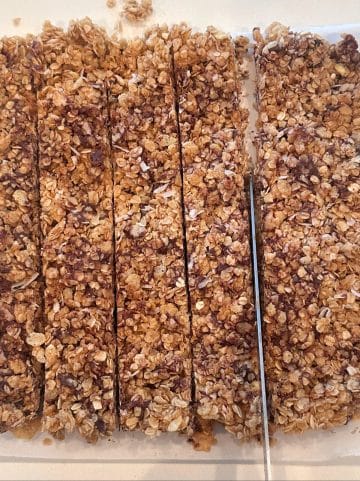 A knife cutting a block of peanut butter chocolate chip oats into granola bars.