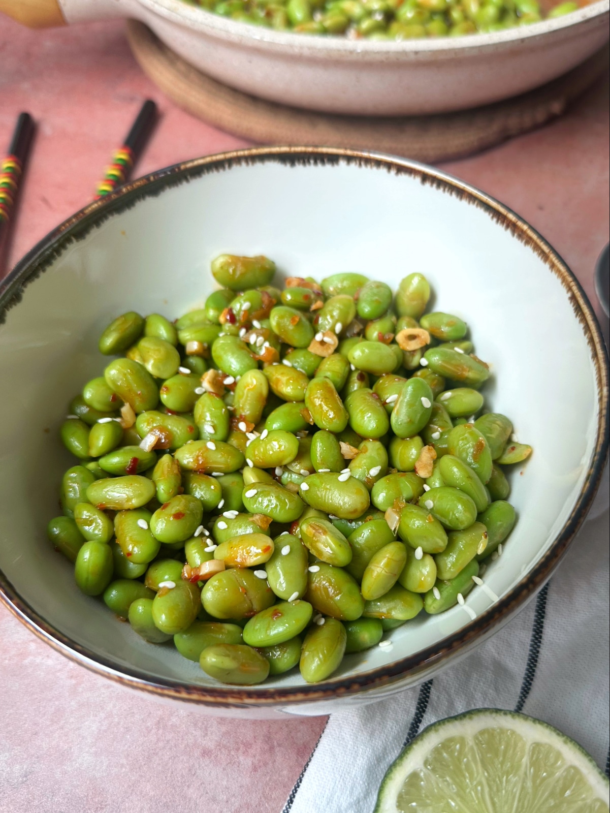 A bowl of shelled edamame with sesame seeds and red chili sauce on top.