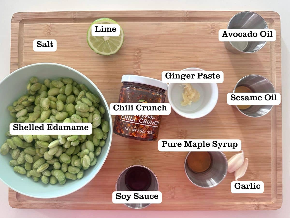 A wooden board containing ingredients for chili lime mukimame, including bowls of soy sauce and ginger paste.