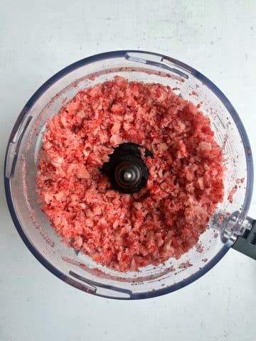 A food processor filled with crushed frozen strawberries.