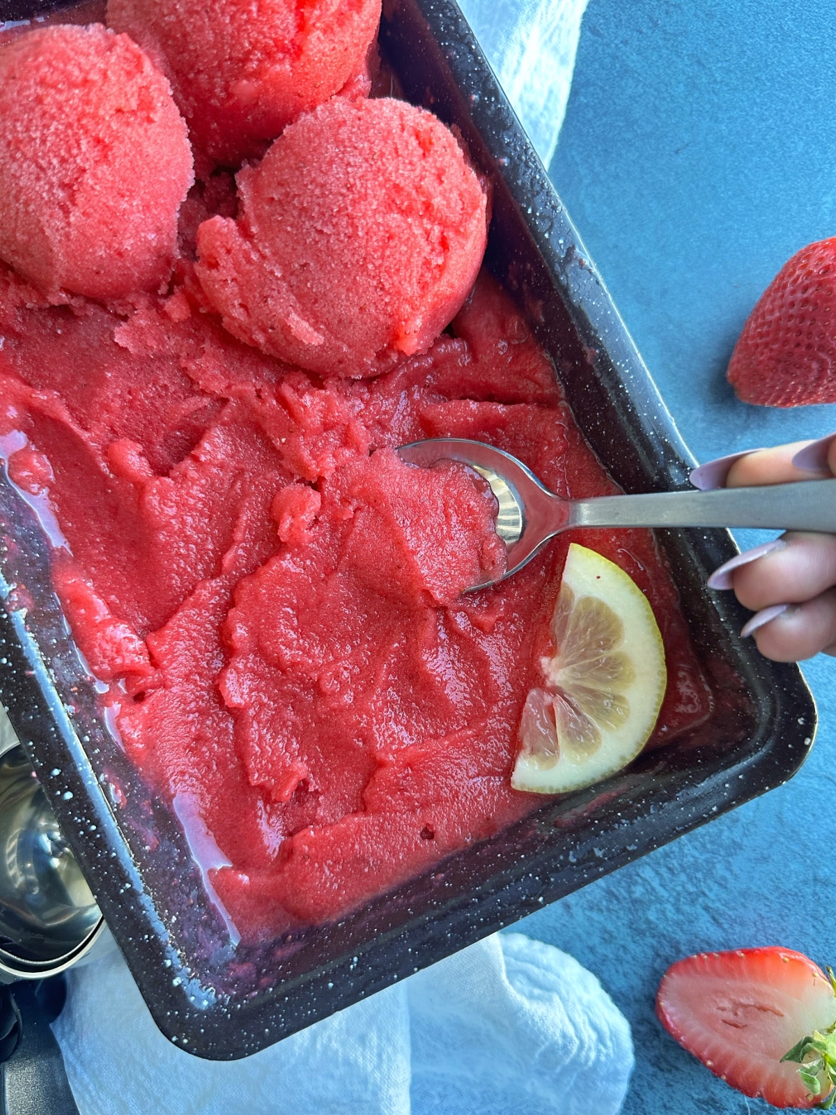 A spoon scooping a bit of strawberry sorbet out of a loaf pan filled with the rest.