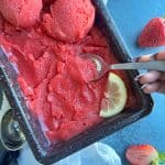 A spoon scooping a portion of homemade Strawberry Sorbet in a black loaf pan.