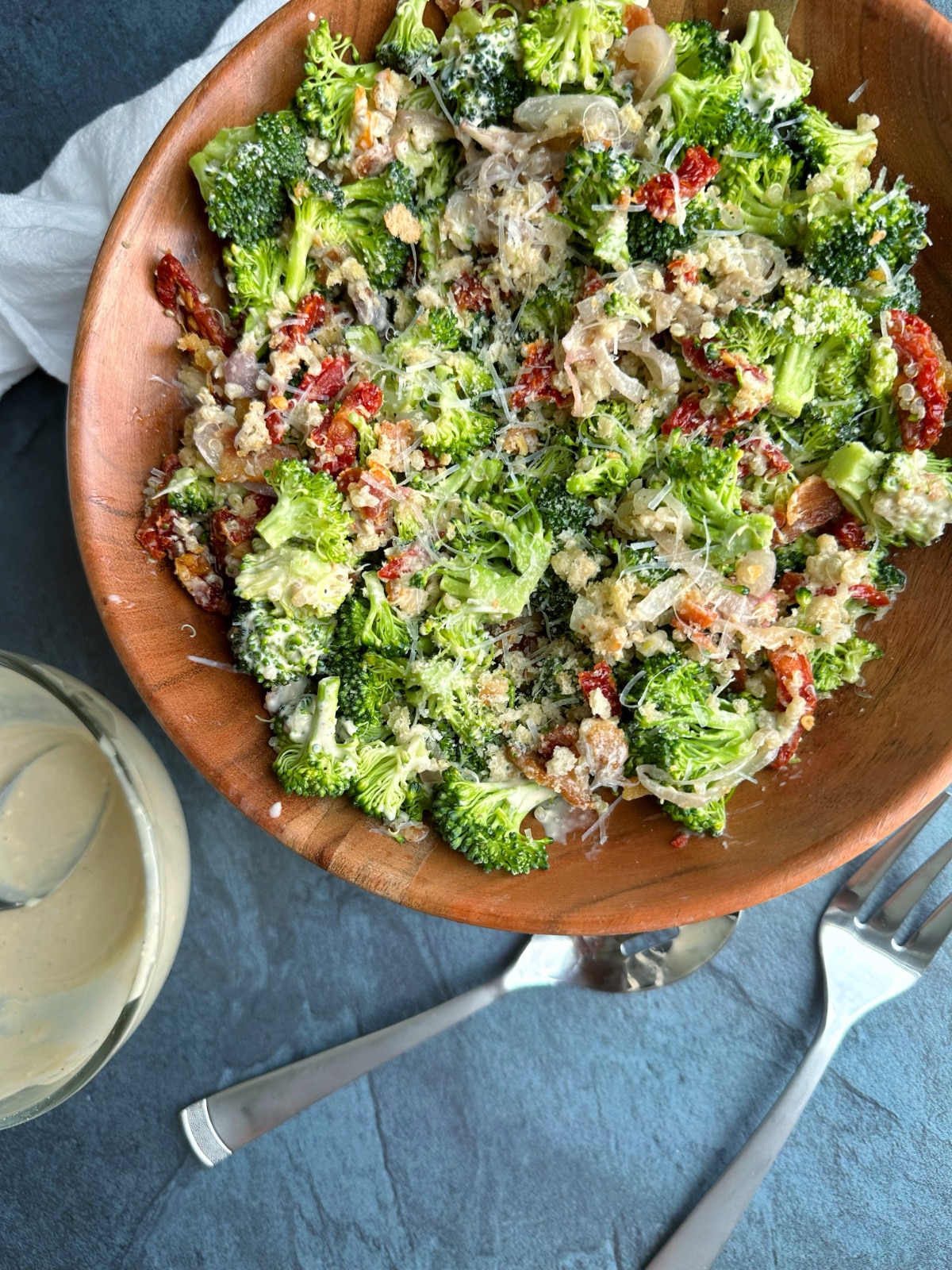 A bowl of Broccoli Salad with bacon, sun-dried tomatoes, quinoa, croutons, shallots, and caesar dressing.