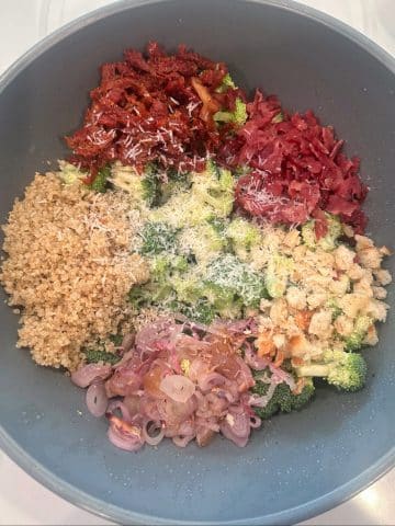 A bowl filled with vegetables, cooked quinoa, bacon, and shredded parmesan.