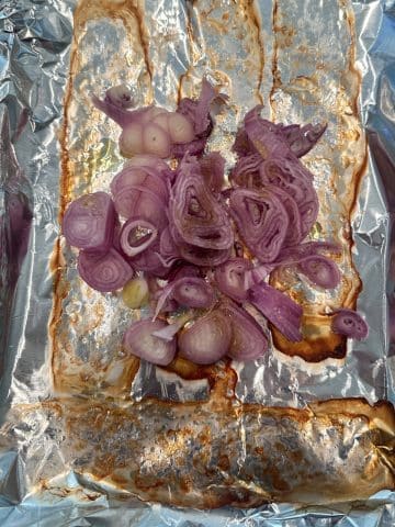 A sheet pan lined with foil, topped with roasted shallots.