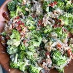 A wooden bowl of Broccoli Salad with bacon, sun-dried tomatoes, quinoa, croutons, shallots, and caesar dressing.
