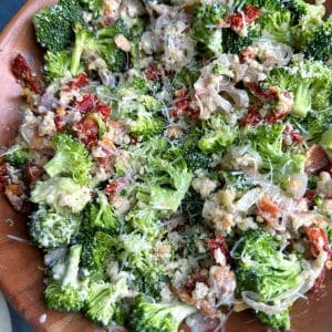 A wooden bowl of Broccoli Salad with bacon, sun-dried tomatoes, quinoa, croutons, shallots, and caesar dressing.