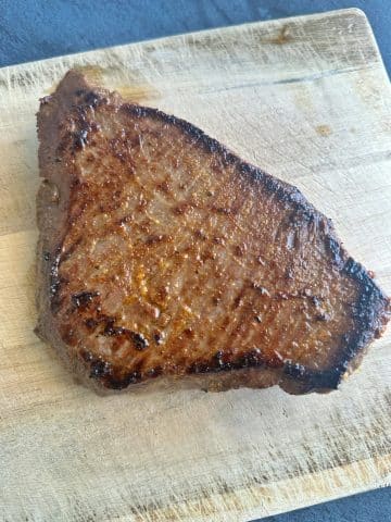 A seared flank steak resting on a wooden board.