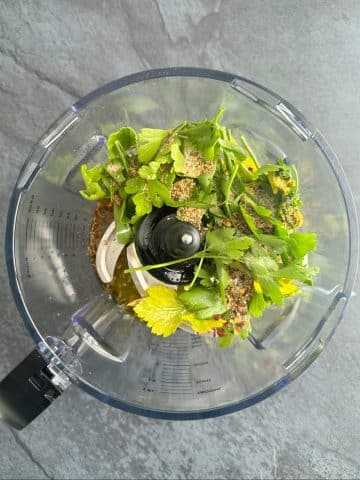 A food processor filled with fresh herbs and spices.