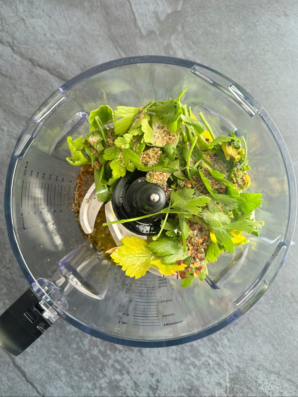 A food processor filled with fresh herbs and spices.
