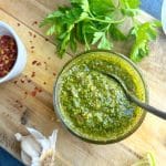 A spoon scooping homemade chimichurri sauce out of a small bowl.