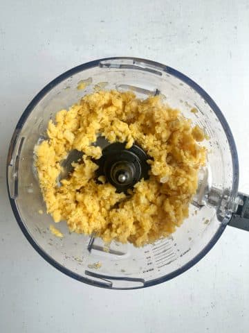 A food processor with small pieces of frozen mango inside.