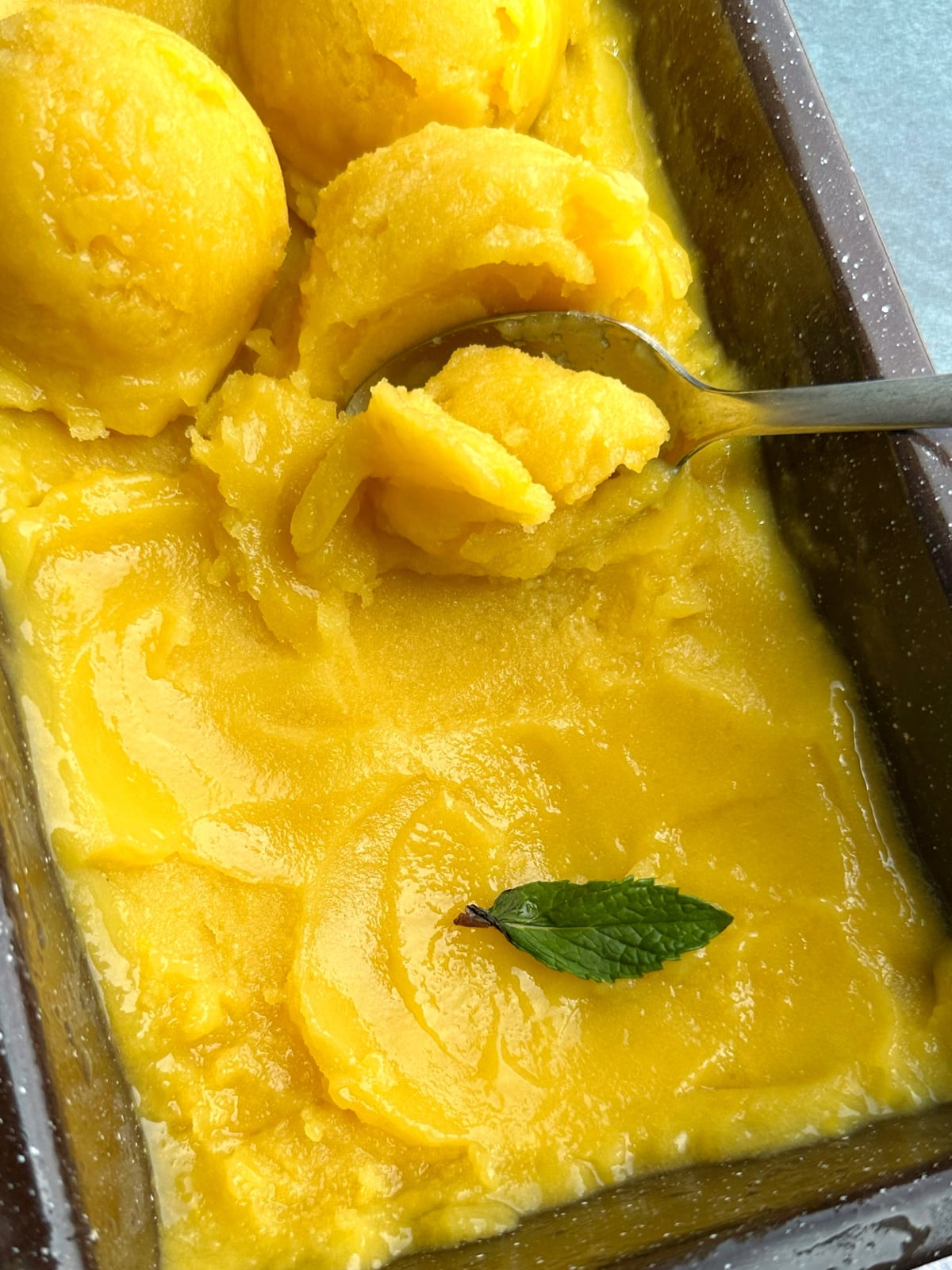 A spoon scooping up some homemade mango sorbet in a loaf pan.