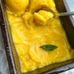 A spoon scooping into Homemade 4-Ingredient Mango Sorbet in a brown loaf pan.