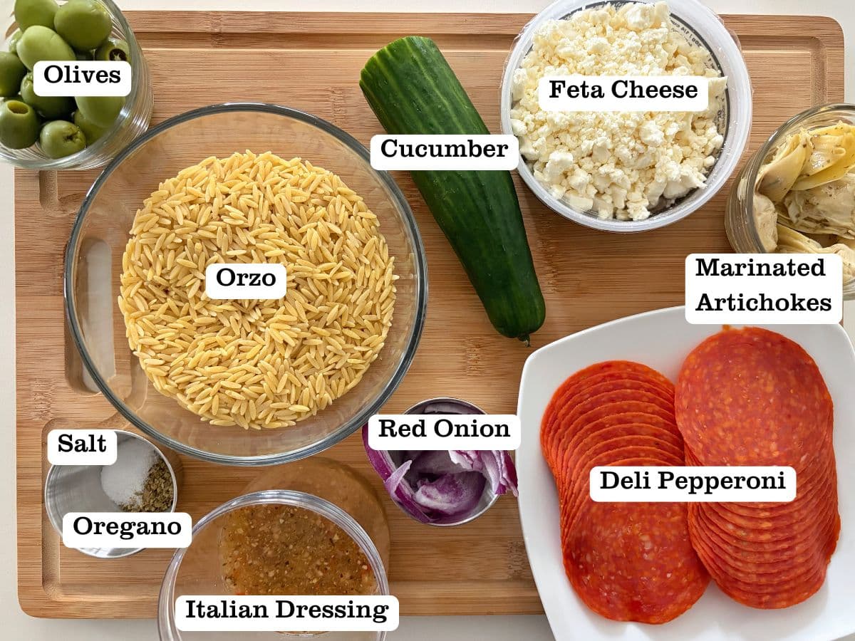 A wooden board containing bowls of ingredients for Italian orzo pasta salad.