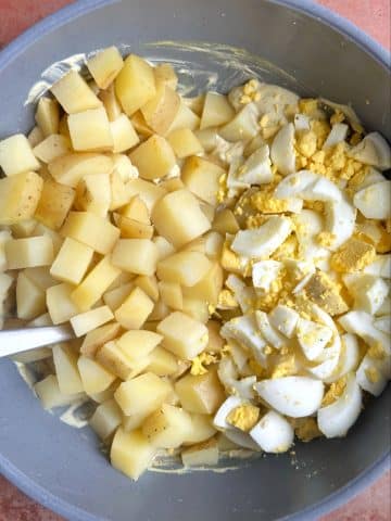 A mixing bowl filled with chopped potatoes and chopped boiled eggs.