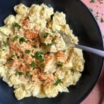 A spoon sticking in a black bowl filled with southern-style potato salad.