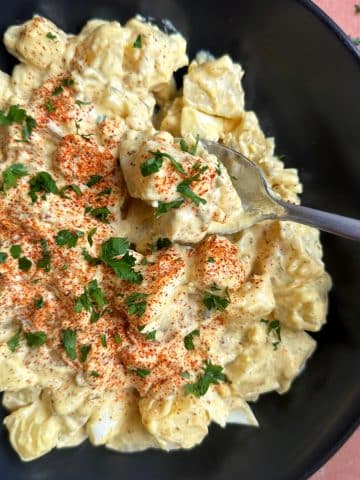 A spoon sticking in a black bowl filled with southern-style potato salad.