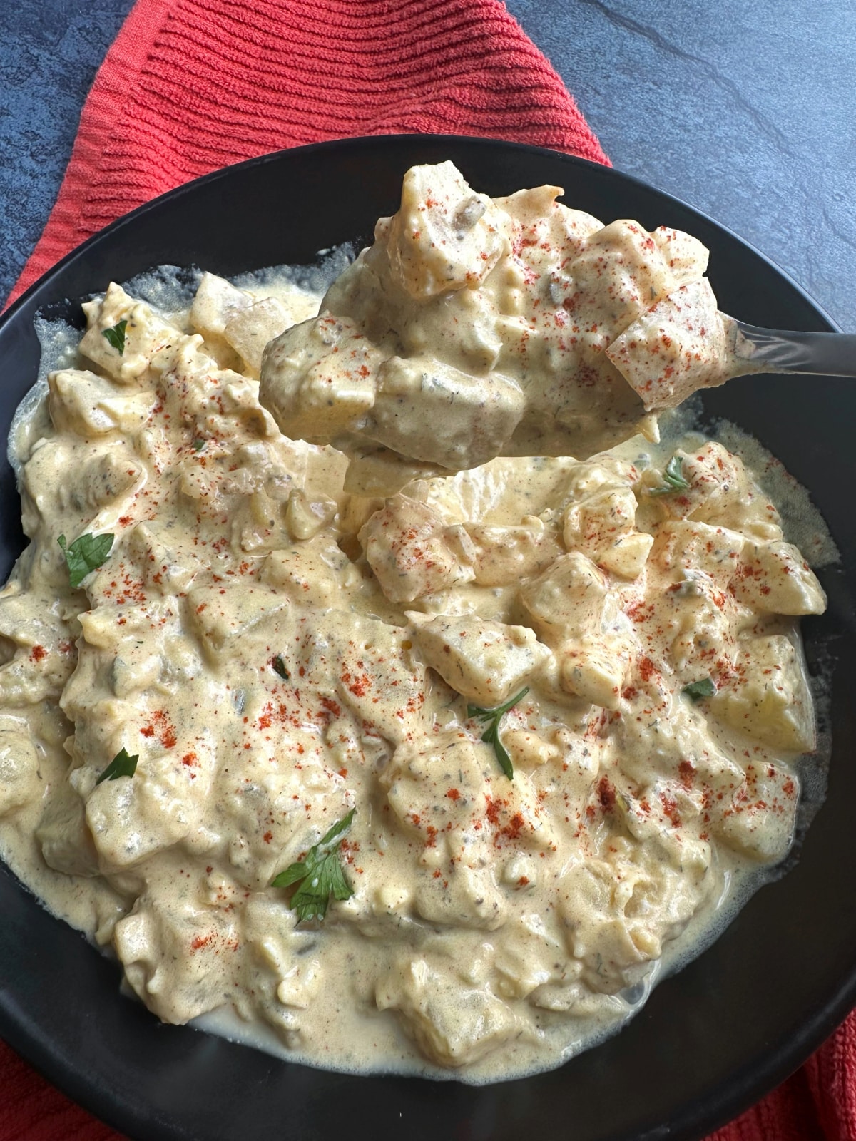 A spoon scooping up classic, southern-style Potato Salad with paprika sprinkled on top.