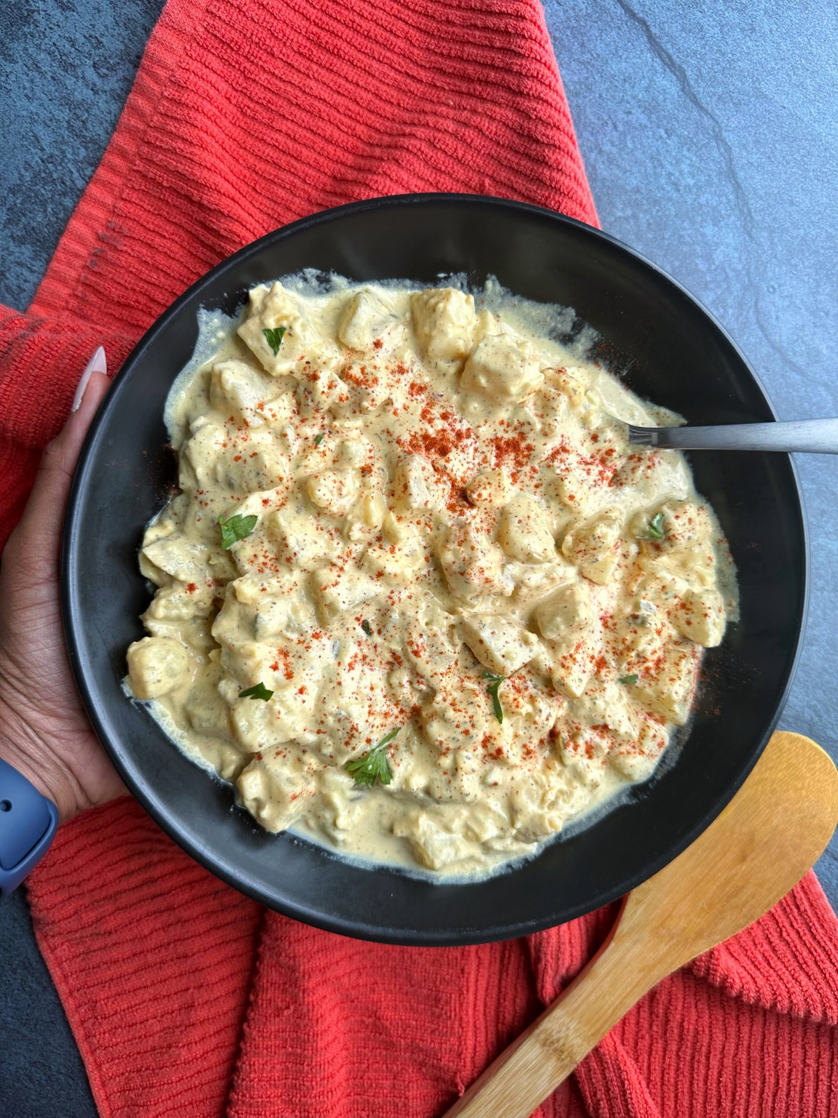 A black bowl filled with classic, southern-style Potato Salad with paprika sprinkled on top and a spoon placed inside.