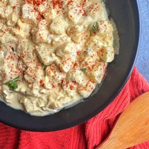 A black bowl filled with classic, southern-style Potato Salad with paprika sprinkled on top.