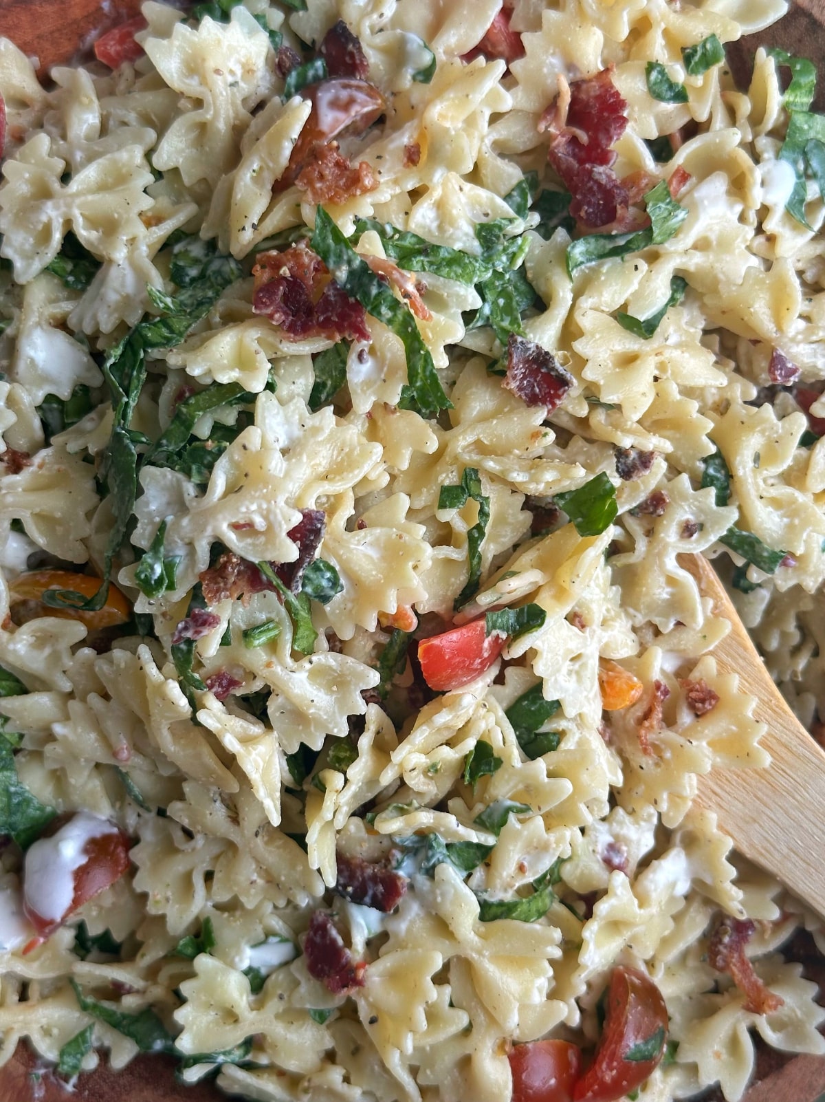 A closeup shot of a bowl of bacon, lettuce, and tomato pasta salad.