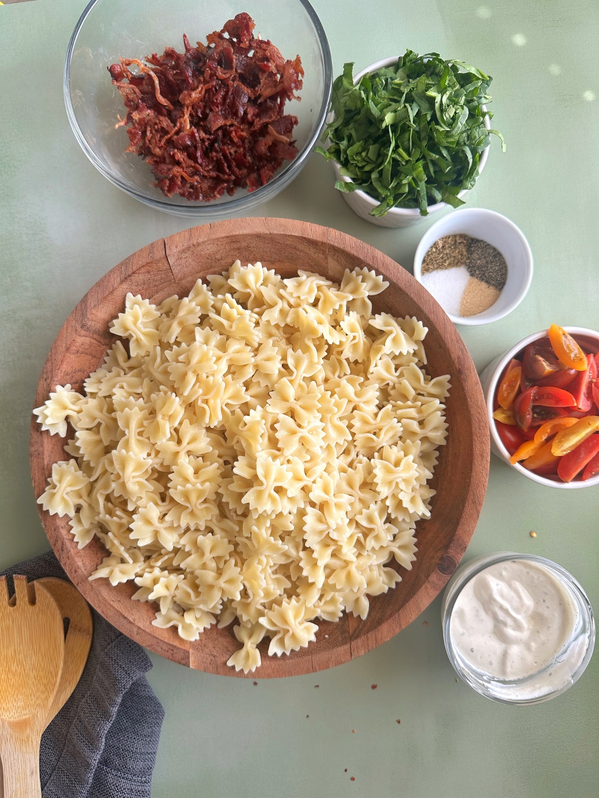 A bowl of cooked pasta surrounded by bowls of other meat and vegetable mix-ins.