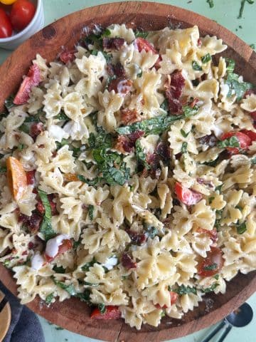 A wooden salad bowl filled with BLT Pasta Salad with serving spoons on the side.