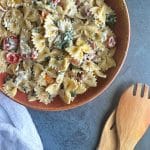 BLT pasta salad in a brown salad bowl with bowtie pasta, beef bacon, grape tomatoes, and spinach leaves.
