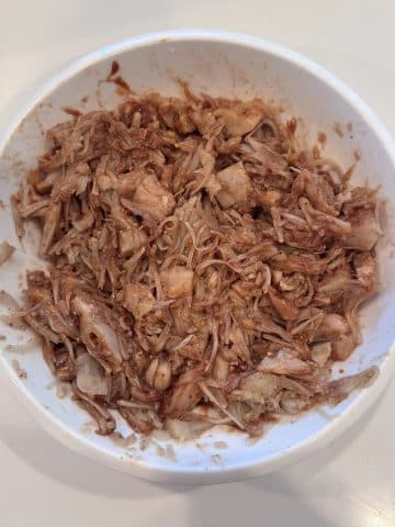 A bowl of shredded canned jackfruit tossed in seasonings and BBQ sauce.