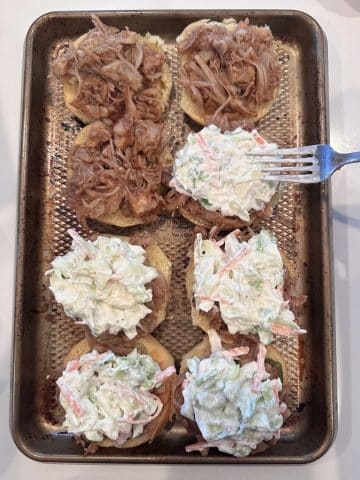 A fork spreading coleslaw onto vegetarian pulled meat sliders.