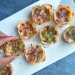A hand grabbing a pizza cup with pepperoni and green bell peppers off of a white serving plate.