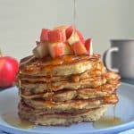 A stack of apple pancakes with chopped red apples and syrup on top.